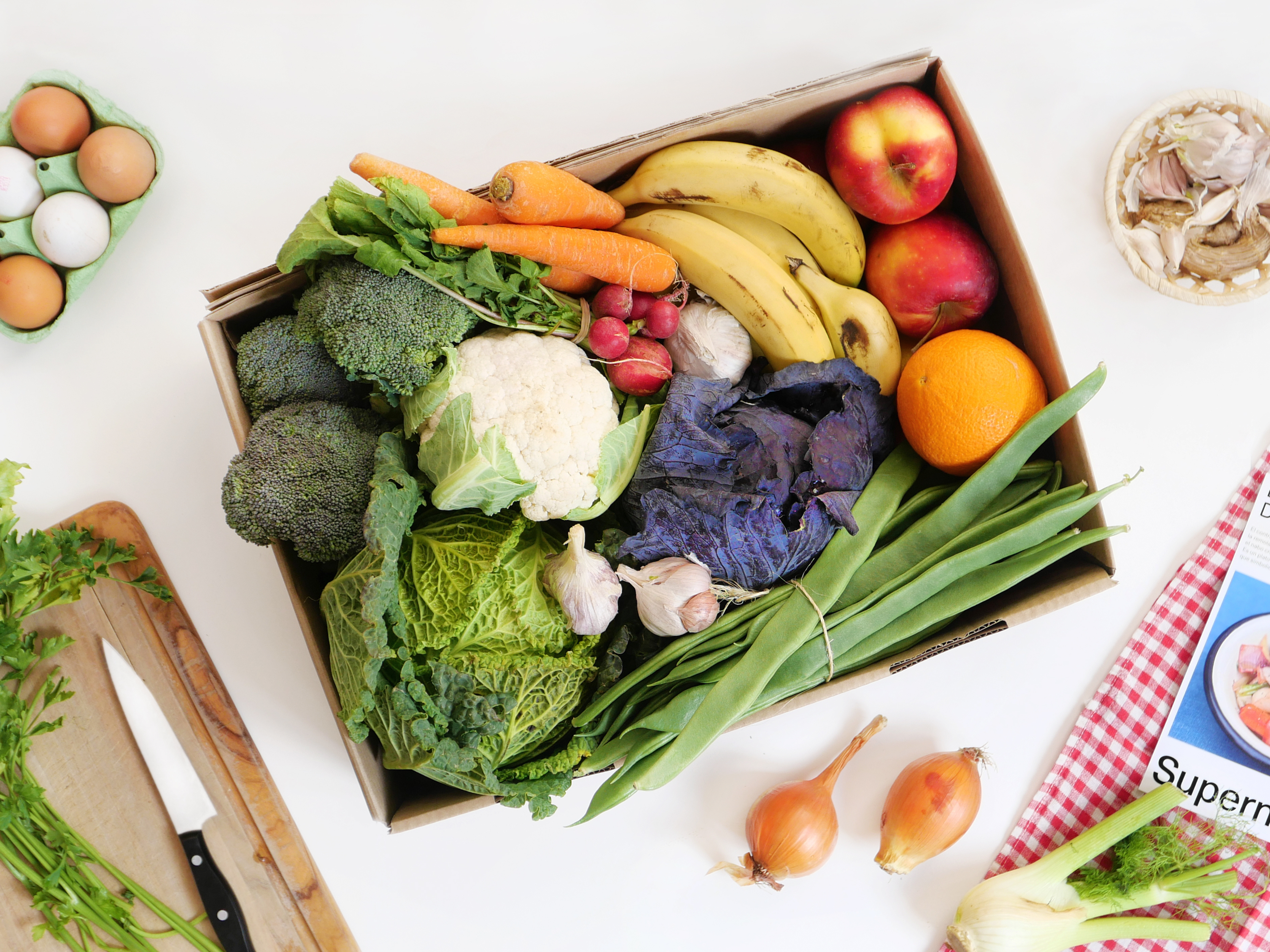 Caja de frutas y verduras sobre mesa blanca